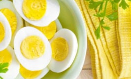 bowl of boiled eggs cut in half with a yellow napkin and green garnish